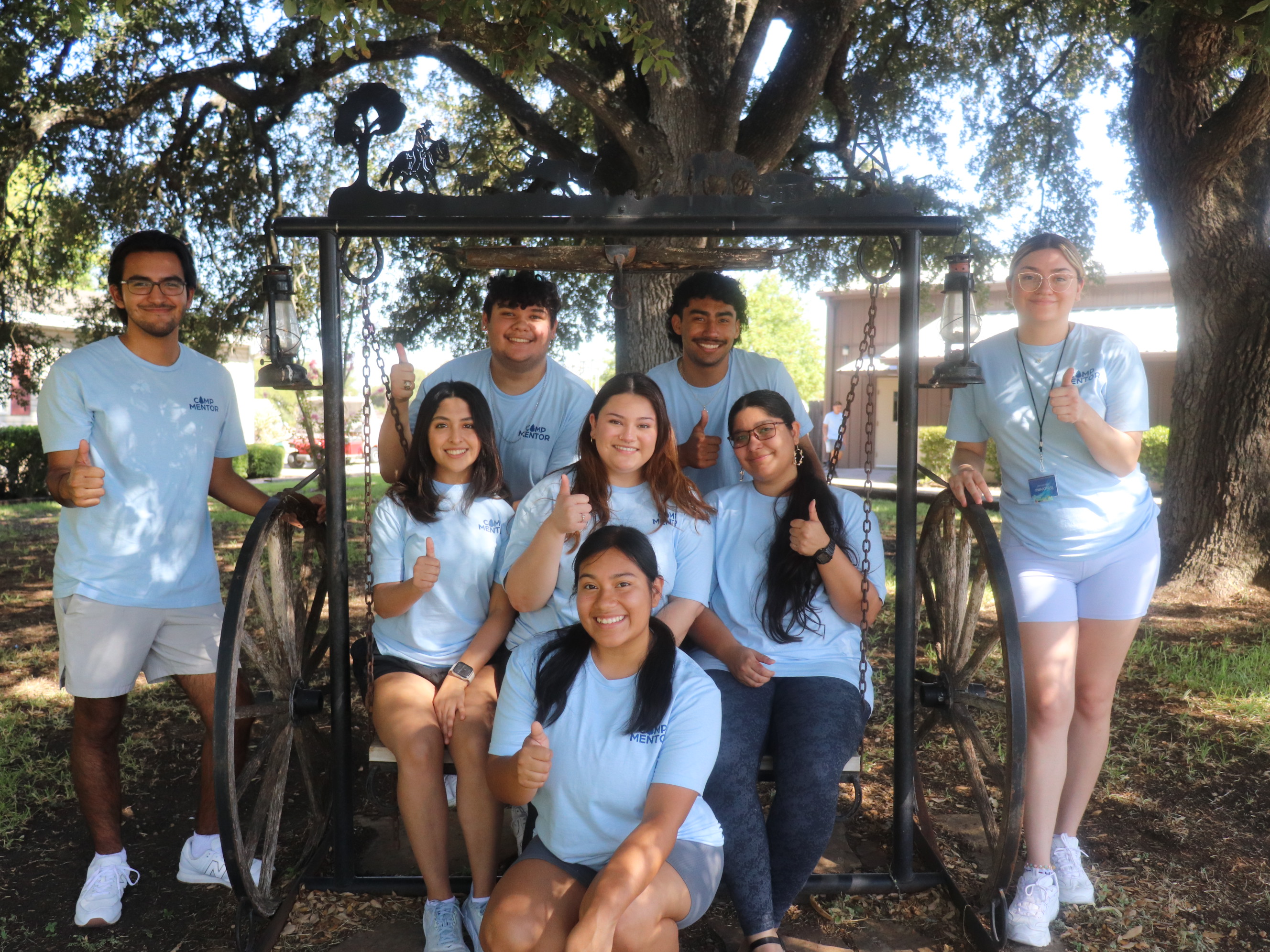 Eight GTF Mentors posing together on a swing while at CAMP Mentor 2023. They are wearing matching blue "Camp Mentor" shirts.