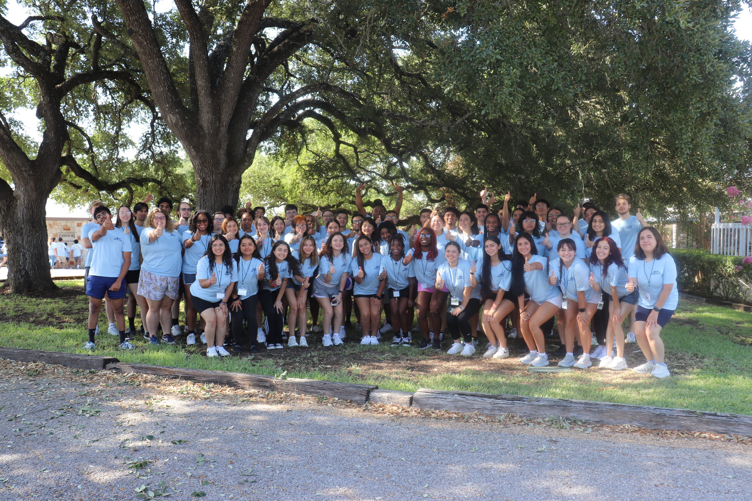 Century Scholars Mentors showing a gig'em hand sign while at Camp Mentor 2023. All 60 of them are wearing matching blue "Camp Mentor" shirts.